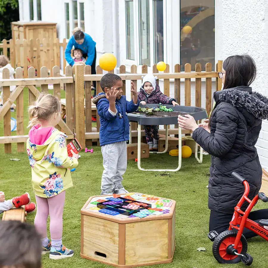 Children playing with a teacher outdoors at Monkey Puzzle Feltham nursery.